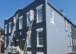 Painters on ladders repainting a townhouse exterior in navy