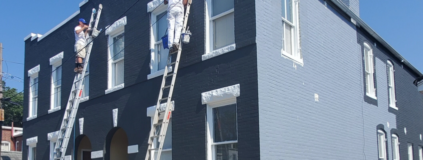 Painters on ladders repainting a townhouse exterior in navy